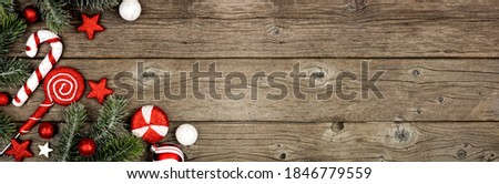 Christmas corner border of red and white decorations with tree branches. Above view on a dark wood banner background with copy space.