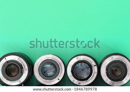 Several photographic lenses lie on a bright turquoise background. Copy space