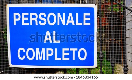 Sign with "complete personal" writing in Italian white writing on a blue background on the gate of a building site, in a sunny day