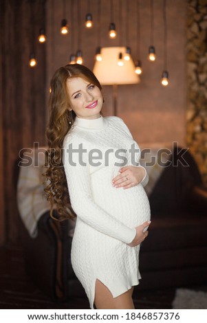Young pregnant woman near christmas fireplace with her Christmas gift. Waiting for baby in New Year eve. Christmas gift for family. Concept image with mum holding her belly with New Year accessories