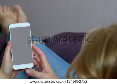 Young woman lies on the couch with a phone in her hand, space for text, close-up