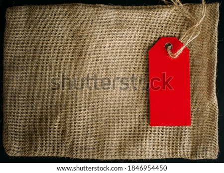 Concept image of an empty label and canvas bag on dark background, copy space. Red tag on a string, close-up.