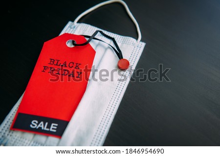 Red tag with the inscription Black Friday on the background of medical mask. Sales in the context of Covid-19 pandemic. Concept of safe shopping.