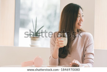 Asian beautiful young woman is smiling, drinking juice while resting at home. Lifestyle Concept.