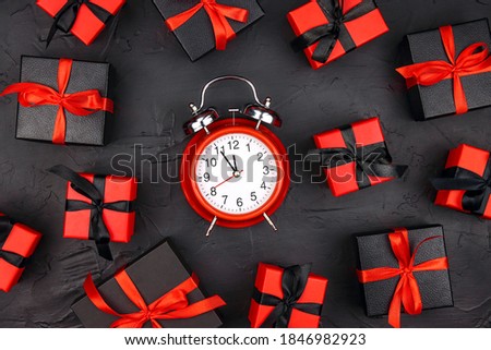 Classic alarm clock surrounded by black and red gift boxes on a black background. Holiday or black friday concept.