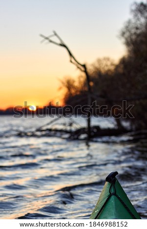 View from a green kayak on autumn brown trees on the banks of the Danube river at sunset on a clear autumn evening. Autumn kayaking.