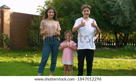 Three young, Caucasian, beautiful teenagers stand on the street and show that they are doing well by raising their thumbs up. Positive emotions. Non-verbal gestures. Everyday leisure. Royalty-Free Stock Photo #1847012296