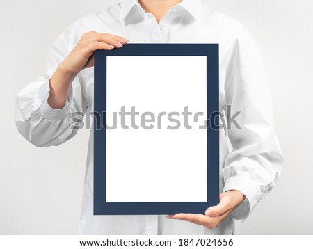 person in white coat holds empty mockup frame. doctor holds and shows the diploma on grey background