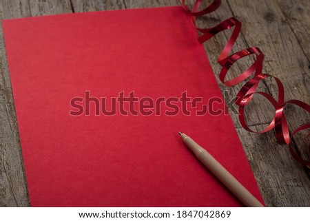 Red sheet of paper for inscriptions and pen on wooden background top view with copy space. 