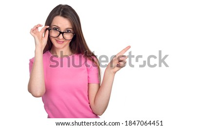 Young woman in pink sweater and glasses points her finger to the right, isolated on white background.