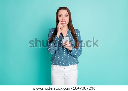Photo of nervous girl hold smartphone her finger touch teeth social network texting concept isolated on turquoise color background