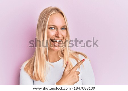 Young blonde girl wearing casual clothes cheerful with a smile of face pointing with hand and finger up to the side with happy and natural expression on face 