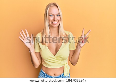 Young blonde girl wearing casual clothes showing and pointing up with fingers number seven while smiling confident and happy. 