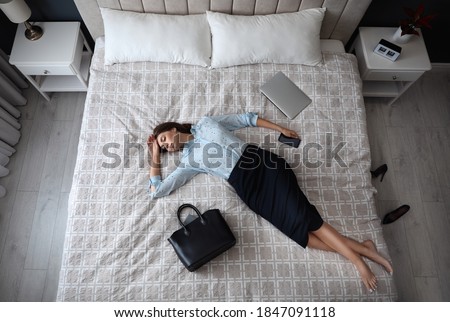 Exhausted businesswoman in office wear sleeping on bed at home after work, above view Royalty-Free Stock Photo #1847091118
