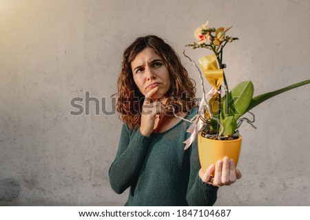Close up young caucasian woman holding a yellow potted orchid plant. Worried face because inexperienced gardener. Royalty-Free Stock Photo #1847104687
