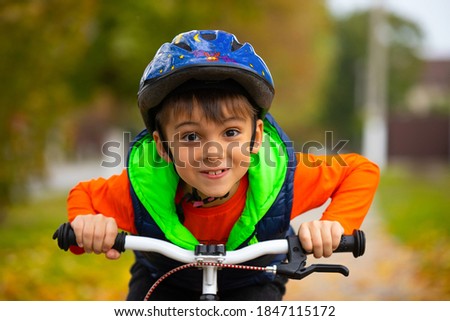 Portrait of a boy posing and smiling in a helmet and on a bicycle pedal in an autumn park. Active healthy outdoor sports. High quality photo