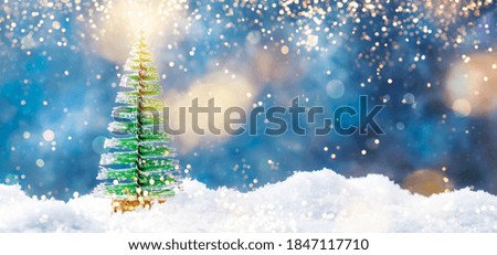 Little Christmas tree toys in snowdrift, winter New Year concept. Festive composition on blue background with lights and snowflakes