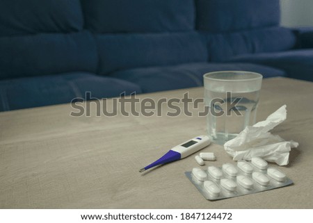 sick kit. thermometer, tissues, pills, medication and glass of water on wooden table
