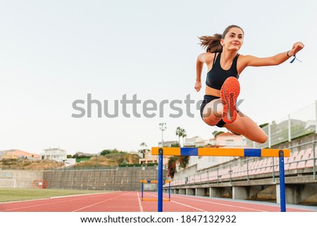 Fit female teenager athlete hurdler running jumping over hurdles Royalty-Free Stock Photo #1847132932