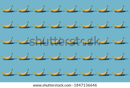 Pattern of yellow bananas with a hard shadow on a blue background. Trendy realistic background.