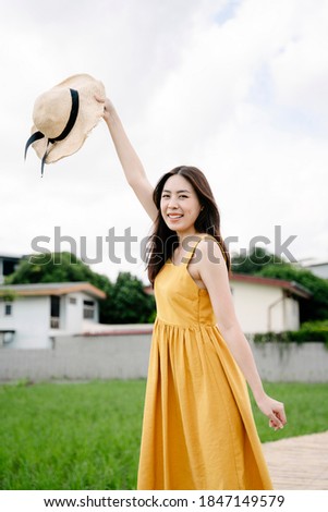 Portrait of beautiful asian traveler woman hold hat standing on wooden bridge across rice field.