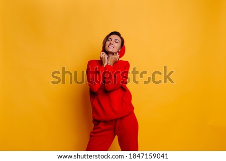 Portrait of happy tanned fit caucasian woman wearing trendy warm red fleece hoodie and pants, getting ready for cold winter. Studio bright shot, yellow background.