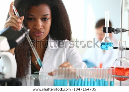 An African woman in laboratory with microscope and liquids in flasks working with them. Outstanding discoveries in chemistry concept Royalty-Free Stock Photo #1847164705