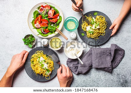 Family lunch table, top view. Peoples hands eating italian pasta with ricotta and fresh vegetables salad. Italian cuisine concept. Royalty-Free Stock Photo #1847168476
