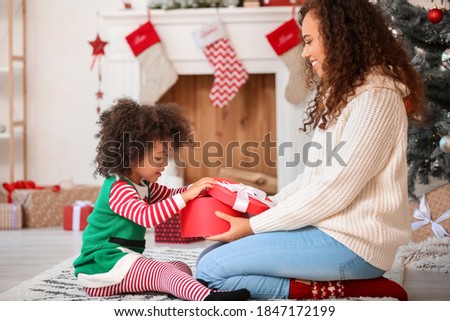 Cute African-American girl and her mother with Christmas gift at home