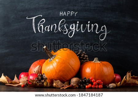Thanksgiving greetings. Pumpkin, leaves, apples on chalkboard background, top view. Kaligraphic capital inscription.