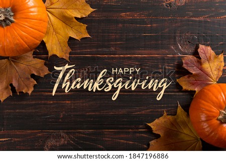 Thanksgiving greetings. Dry yellow leaves, pumpkins, berries, nuts and frame on wooden background, top view. Kaligraphic capital inscription.