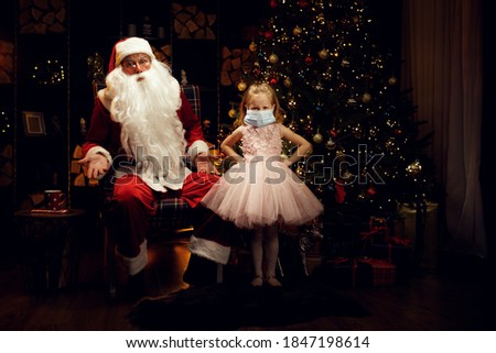 Santa Claus and little angry little girl make her wear a medical mask in Christmas Holidays and pandemic.