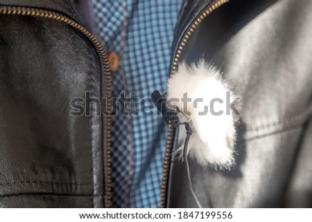 Microphone lapel pin with wind protection on a leather jacket.