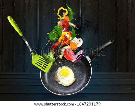 Healthy eating and cooking with various flying chopped vegetables ingredients,wooden table, pan with chicken isolated on black background, front view. Concept diet and healthy eating.