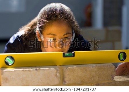 A young Bricklaying student in a vocational school using the spirit level on a brick wall while closely watching the alignment of the bricks Royalty-Free Stock Photo #1847201737