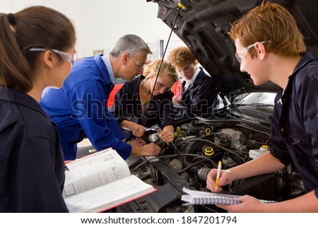 A side view of a trainer closely watching his student repair a car in a vocational school of automotive trade Royalty-Free Stock Photo #1847201794