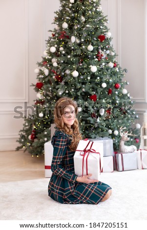 Young girl in dress sit on floor with Xmas gifts in living room. Little girl opening magical christmas present at home. Merry Christmas and happy holidays. New Year. Christmas interior room