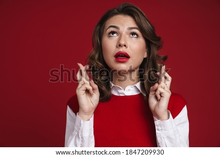 Photo of a concentrated young woman showing fingers crossed gesture isolated over red wall background