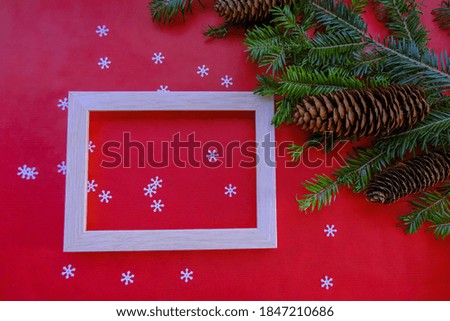christmas greeting card with picture frame across christmas tree branch, cones,  tinsel on red background. Top view. Copy space