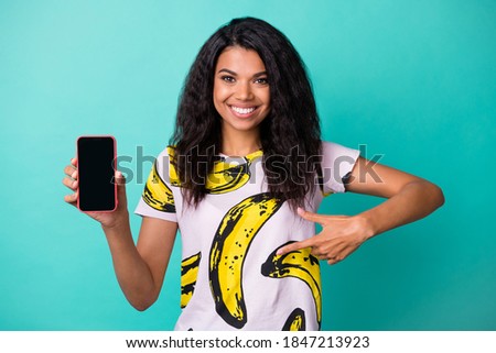 Photo of cute young girl hold smartphone screen empty space direct finger wear banana print t-shirt isolated teal color background