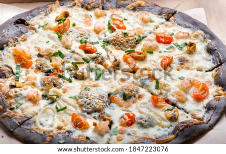 Delicious pizza on black dough with cheese mozzarella , tomatoes, seafood and green onion. Top view, close up.