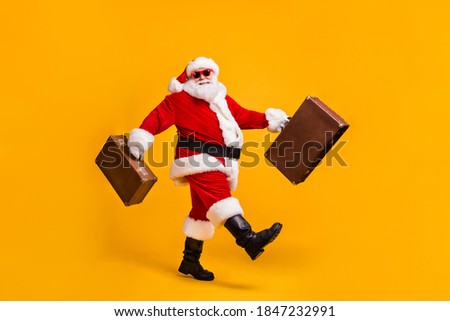 Full body profile side photo of white grey hair bearded santa claus go carry luggage x-mas christmas eve noel trip wear cap sunglass boots isolated yellow shine color background