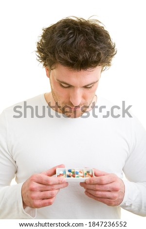 Young man looks at pill box labeled morgens-mittags-abends-nachts (German for: morning-noon-evening-night)
