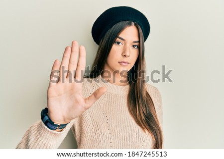 Young brunette woman wearing french look with beret doing stop sing with palm of the hand. warning expression with negative and serious gesture on the face. 