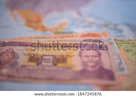 Close up picture of banknotes of one, five, and two Honduran lempiras -with the words Republic of Honduras and Central Bank of Honduras in Spanish- under Honduras on a blurry Central America map