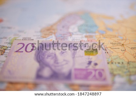 Close up picture of a twenty Swedish kronor banknote -with the words Twenty Kronor in Swedish- below Sweden on a colorful and blurry Europe map
