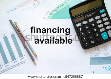 Business reports, blank paper sheet, data tables and charts - directly above view of office table workspace with FINANCING AVAILABLE text. High quality photo