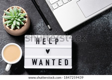 Office desktop with lap top, succulent flower, coffee with milk and Help Wanted text on the lightbox. Concept of hiring and recruitment.