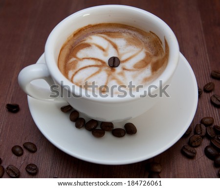 A cup of cappuccino and coffee beans on old wooden background 