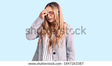Young beautiful blonde woman wearing call center agent headset tired rubbing nose and eyes feeling fatigue and headache. stress and frustration concept. 